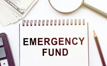 An emergency fund notebook, pencil, calculator, magnifying glass, and cash