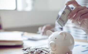 A hand placing a hundred dollar bill in a piggy bank.